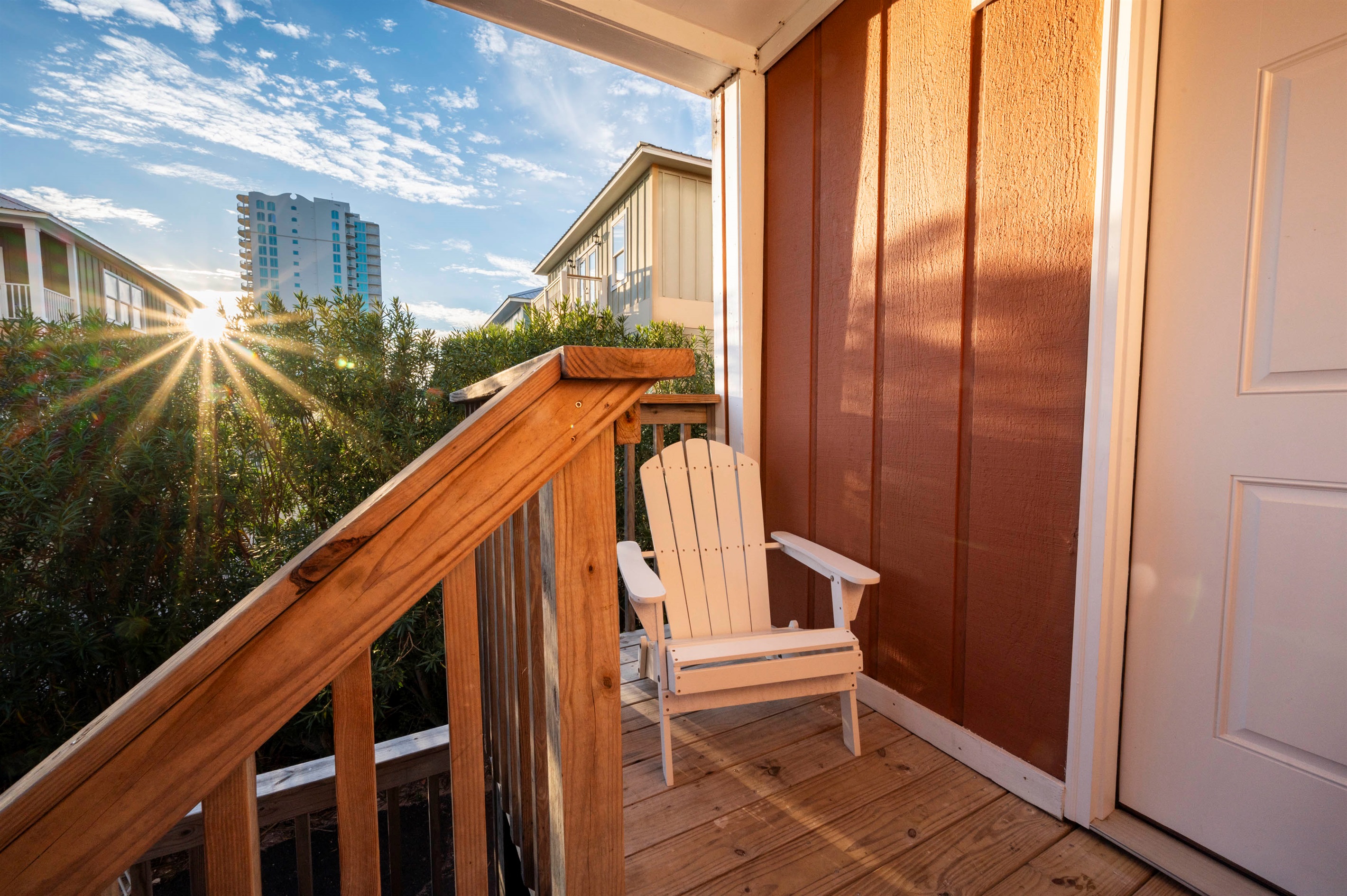 Experience the serene sunset glow on a cozy porch with a white chair and a view of lush greenery.