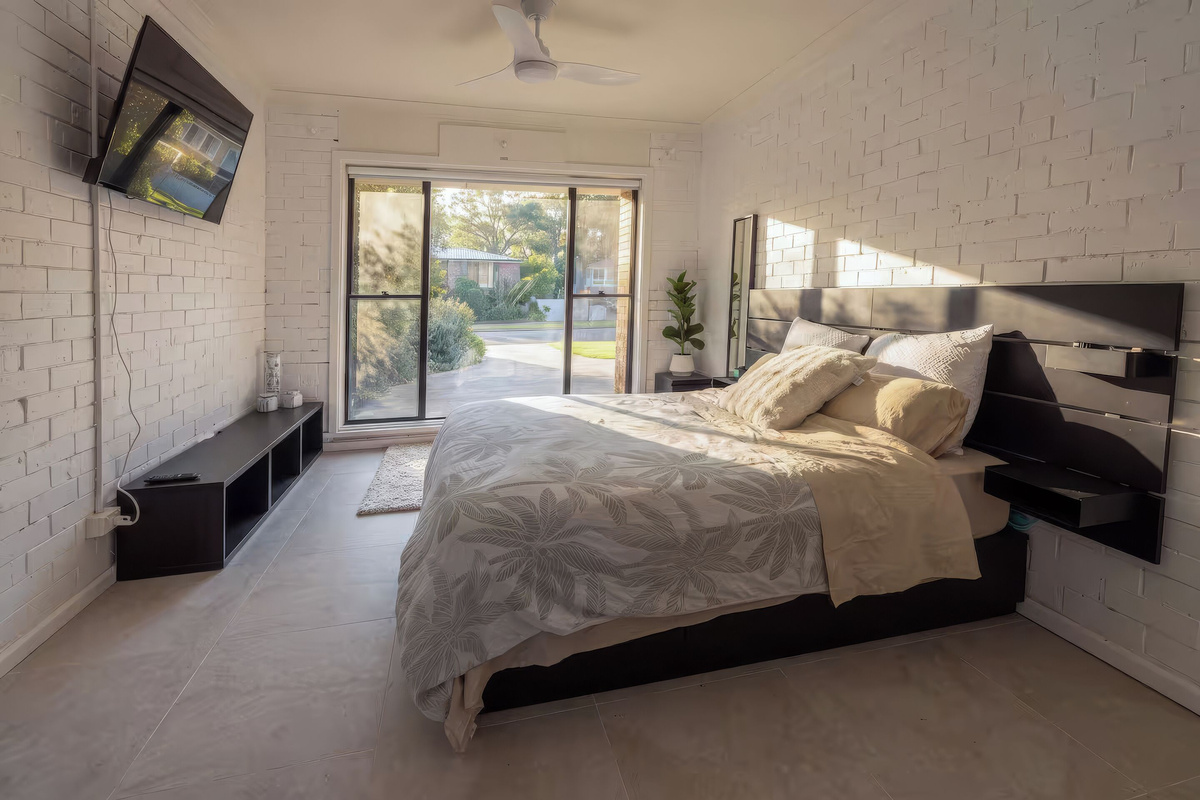 This queen bedroom at Luna’s Sanctuary features a ceiling fan, wall-mounted TV, sliding glass doors and a garden-facing outlook.