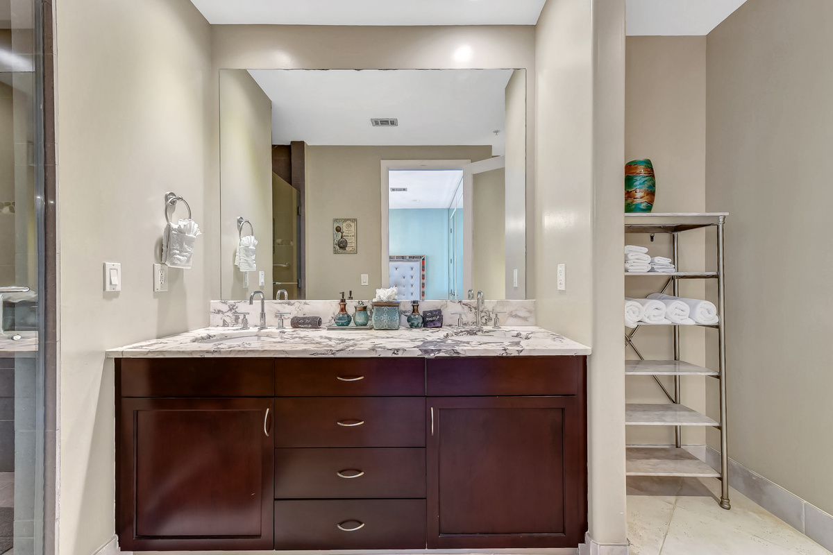 Master bathroom with double-sinks and walk-in rain shower.  The rain shower has a handrail and a portable shower chair.  