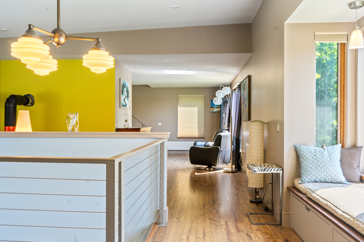 Architectural details at "The Crag." A cozy built-in window reading nook anchors the open upper hallway, featuring stylish mid-century lighting, rich hardwood floors, and bright accents leading into the main living spaces.