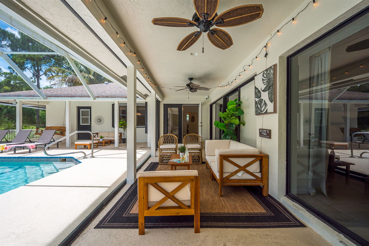 Screened-in pool area with heated pool and spa, surrounded by lush greenery. Features ample lounge seating, BBQ grill, and cozy covered patio with outdoor dining and relaxing sitting area.
